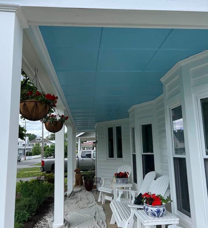 Front porch in Solomons Island, Maryland, finished by Gray & Sons Contracting with white columns, trim, and siding under a painted blue porch ceiling